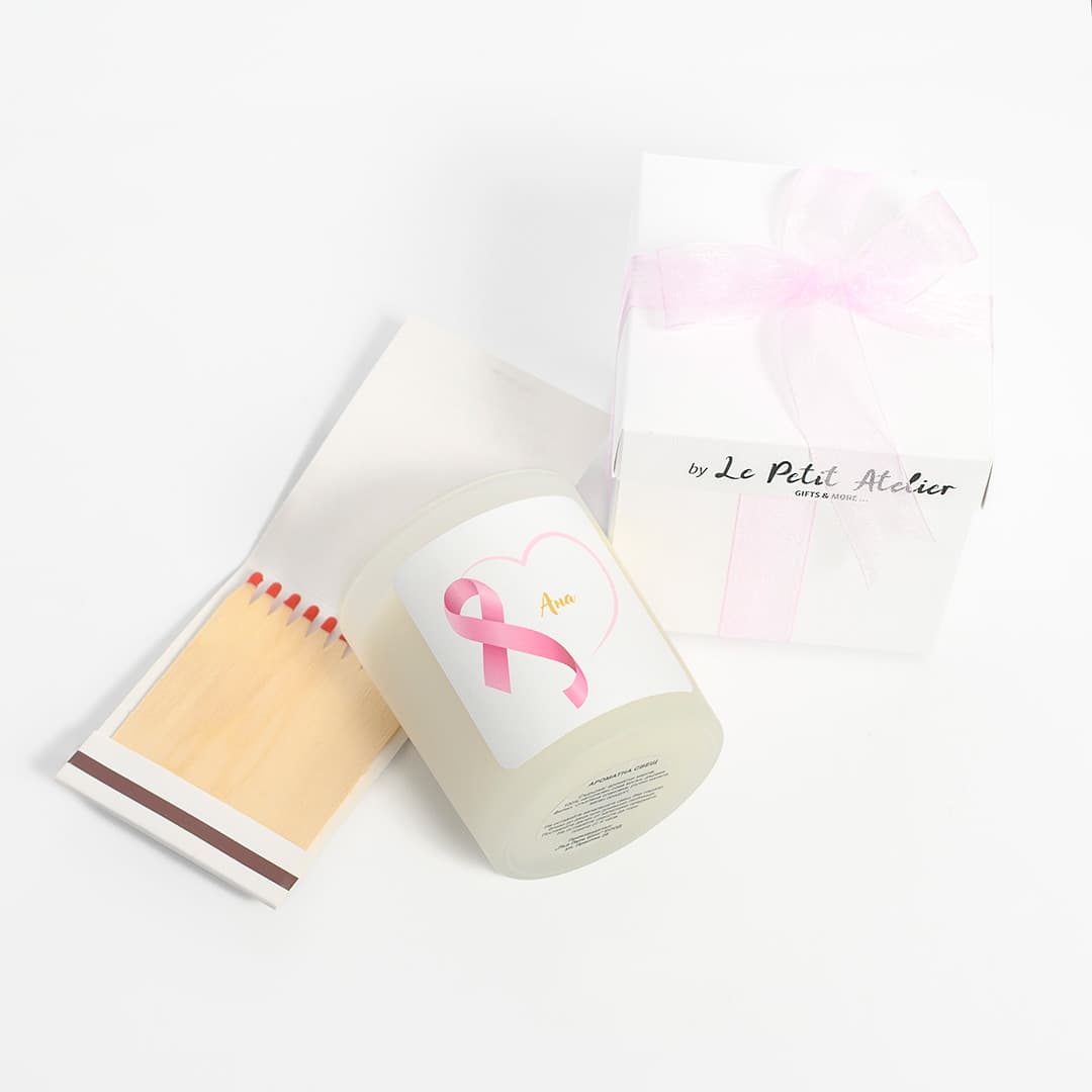 Weiße Geschenkbox mit rosa Schleife, personalisierte Kerze mit Brustkrebs-Symbol und geöffnete Packung Streichhölzer.