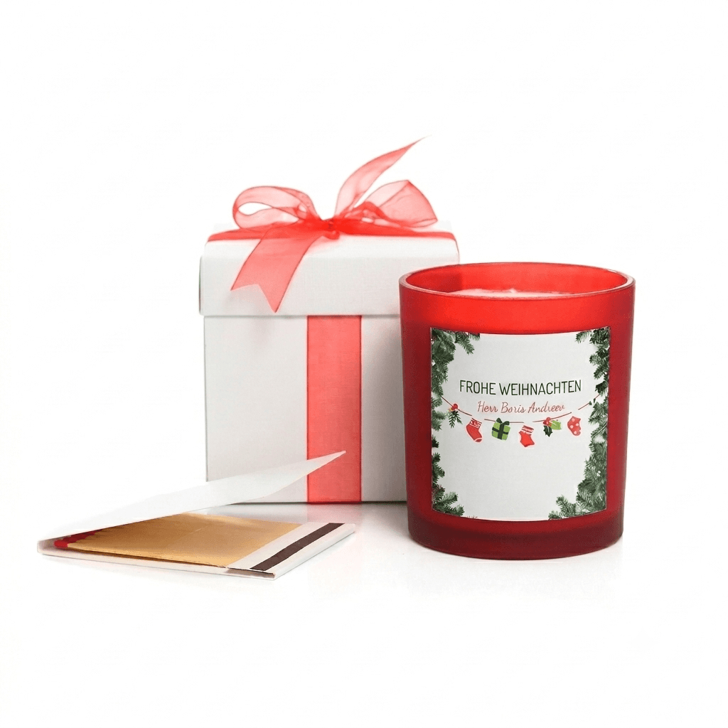 Rote Weihnachtskerze mit personalisiertem Etikett neben einer weißen Geschenkbox mit roter Schleife und Streichhölzern.