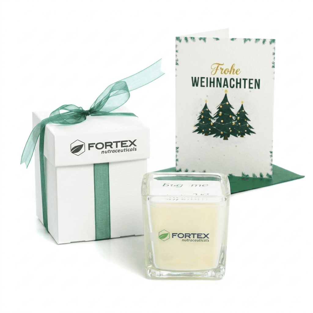 Weiße Geschenkbox mit grüner Schleife, Logo-Kerze und Weihnachtskarte mit der Aufschrift Frohe Weihnachten.